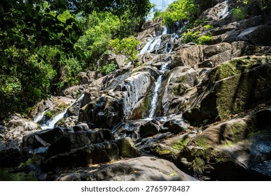 A small waterfall flows over large rocks beneath dense green vegetation near Kibale National Park in western Uganda. Moss covers parts of the boulders around the stream