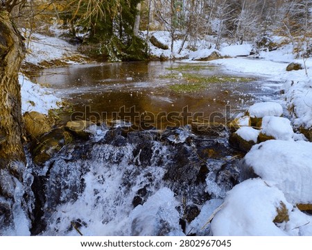 Small waterfall in a forest stream with flowing water, ice formations and snow-covered rocks on a cold winter day, photographed in the Vitosha Mountains near Sofia, Bulgaria.