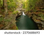 A small waterfall pours into a wide deep pool in Roaring Brook, Scranton PA. The pool is surrounded by cliffs with trees just beginning to turn to autumn colors above it all.