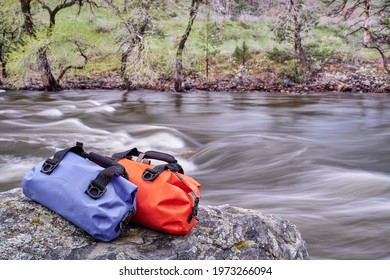 small waterproof duffels on a rocky river shore - Poudre River in a canyon above Fort Collins, Colorado, in springtime scenery