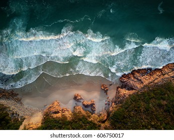 Small Waves Repeatedly Crashing On Small Sandy Shore Bay Beach With Rough Rocky Coastline, Aerial Photography Overhead