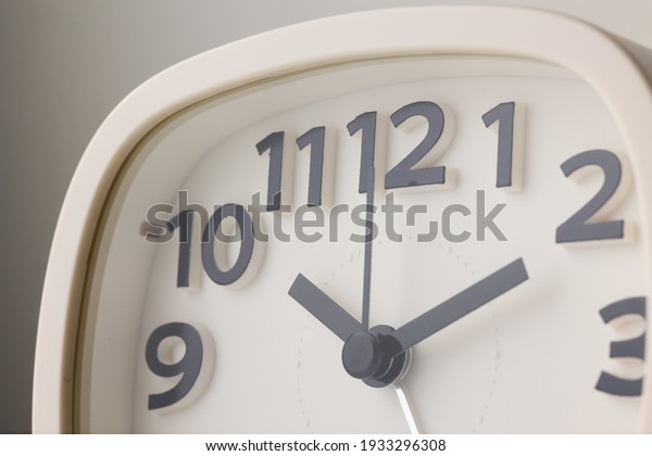 Small white alarm clock, black\
numbers, set the time for 10.10 o\'clock, placed on a white\
table.
