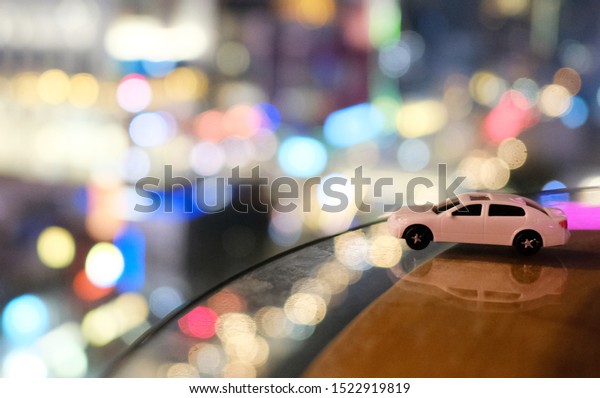 Small\
white car toy with city, nightlife with\
bokeh.