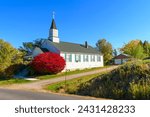 A small white church with a bright red bush showing fall colors at autumn in the rural countryside of Green Bluff, near Spokane, Washington USA.