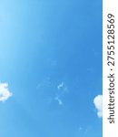 Small white cloud patches float within a bright blue sky, photographed from a low angle in daylight. The composition uses broad negative space and soft natural light to create a minimal atmospheric background.