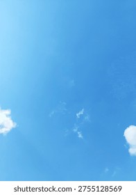 Small white cloud patches float within a bright blue sky, photographed from a low angle in daylight. The composition uses broad negative space and soft natural light to create a minimal atmospheric background.
