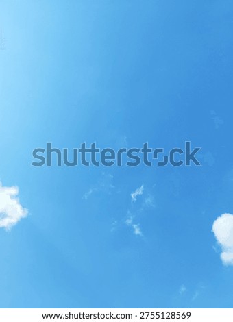 Small white cloud patches float within a bright blue sky, photographed from a low angle in daylight. The composition uses broad negative space and soft natural light to create a minimal atmospheric background.