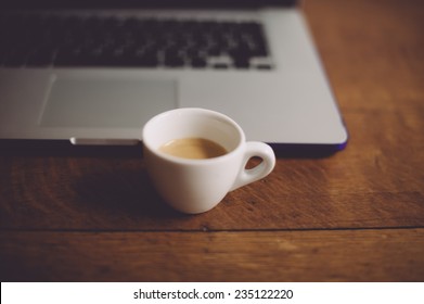 Small white demitasse cup of fresh morning espresso coffee with a beautiful crema with the laptop on the background - Powered by Shutterstock