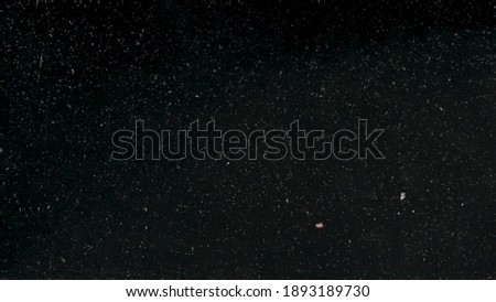 Small white dust particles floating slowly underwater on black background. Action. Tiny particles looking like white snowflakes falling at night.