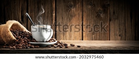 Small White Espresso Cup With Heart Shaped Handle On Wooden Table With Burlap Sack And Coffee Beans