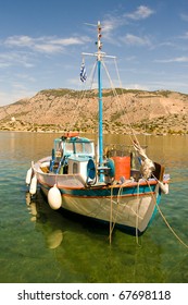 A small white fishing boat standing at a pier in a Mediterranean bay surrounded by mountains