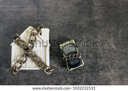 Small white house, car and a decorative chain on a dark background. Concept  -  risks, lose property,  seize, mortgage.
