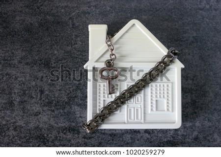 Small white house, chain and a decorative key on a dark background. Concept  -  risks, lose property,  seize, mortgage.