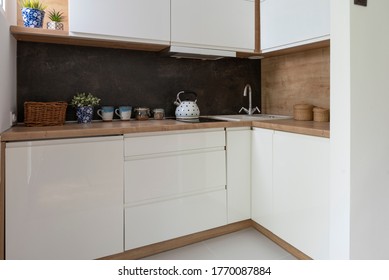 Small White Kitchen With Bright Furniture And Dark Marble, Wooden Counter, Plant And Kettle. Simle Interior Of Kitchen.