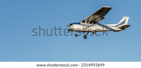 Small white plane with blue stripes of a cessna propeller flying from side view point of view in a clear blue cloudless sky before landing at Sabadell airport.
