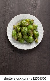 Small White Plate Of Cooked Green Brussel Sprouts On Dark Wooden Background Above Shot