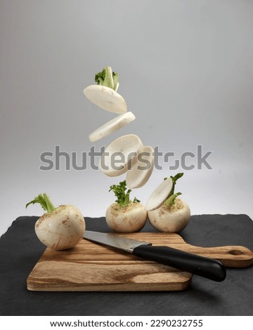 Small white round snowball radish on white background cut sliced diced stacked wooden chopping board knife marble slate stone elevated flying drop falling 