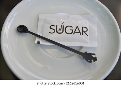 Small White Sugar Pack On A Coffee Tea White Plate With Small Plastic Spoon 