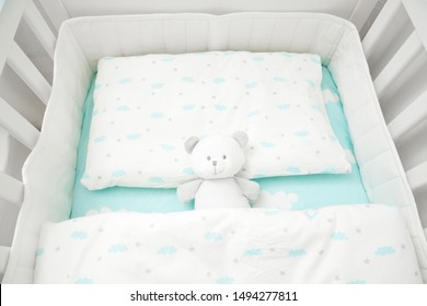 Small, white teddy bear in baby bed. Linen with clouds. 