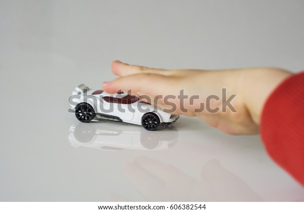 Small white toy car, pushed by children\'s hand.\
The hand is defocuses