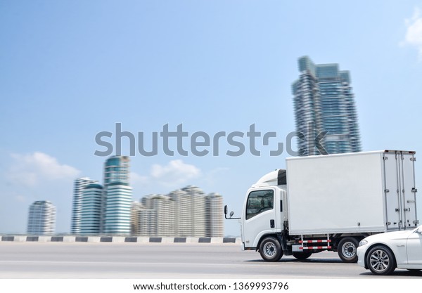 A small white truck running on\
the road for a transportation business with a city\
background.