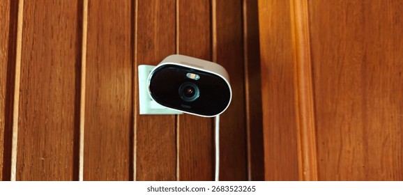 Small Wi-Fi security camera mounted on a wooden wall inside a home, power cable visible.