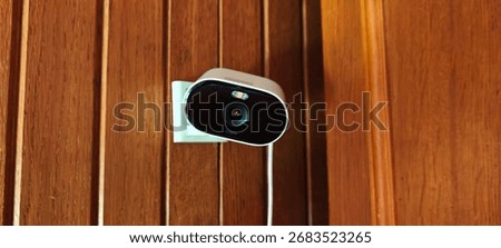 Small Wi-Fi security camera mounted on a wooden wall inside a home, power cable visible.