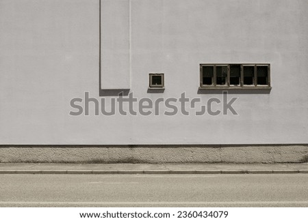 Small windows on gray plaster facade. Concrete sidewalk and urban street in front. Background for copy space.