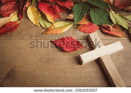 Small wood cross with a border of autumn leaves on a wood background with copy space 