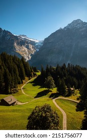 Small Wood House In Sunny Valley Surrounded Snowy Switzerland Alps.