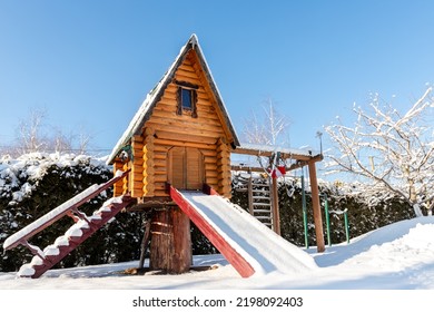 Small Wood Log Playhouse Teehouse Hut Snowcapped Stairs Ladder Wooden Slide Children Playground At Park Or House Yard. White Snow Covered Lodge Blue Clear Sky Background On Bright Sunny Winter Day