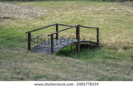 a small wooden bridge over a small dry canal. wooden bridge on a green clearing with a dry stream.