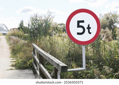 Small wooden bridge with weight limit sign indicating maximum vehicle load of 5 tons. Rustic structure across water or road in countryside. Rural pathway with traffic regulation for heavy vehicle. - Powered by Shutterstock