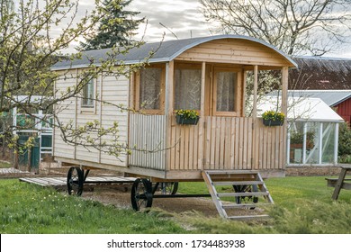 Small wooden caravan parked in the garden. Nice home made travel home on wheels. Caravan park in the sunset. Small cottage house with sauna. Static home. Outdoor living space. Modern caravan home