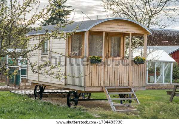 Small wooden caravan parked in the garden. Nice home\
made travel home on wheels. Caravan park in the sunset. Small\
cottage house with sauna. Static home. Outdoor living space. Modern\
caravan home