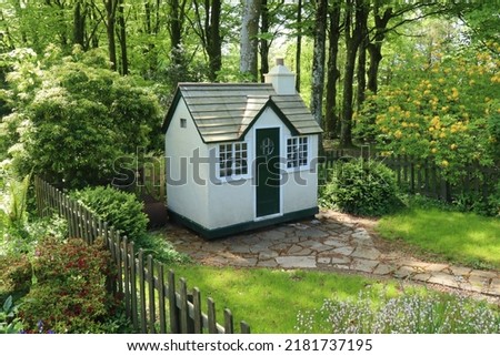 A small wooden children's play house in it's own little garden surrounded by a picket fence