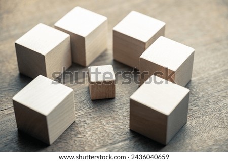 A small wooden cube under siege by many big wooden cubes, concept of a small business encircled by many big ones, high competition, or niche market
