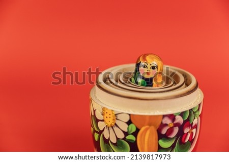 A small wooden doll inside a set of large matryoshkas. Open Traditional Russian symbol opposite the red background