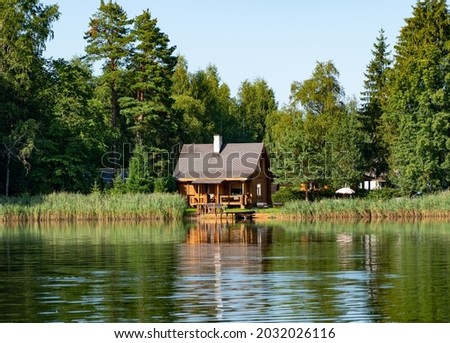 Small wooden fishing or sauna hut by the calm lake in middle of the forest. Small log cabin  near the bond. Perfect sunny warm summer day in Estonia. Amazing reflection on the lake.