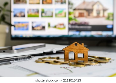 A small wooden house with coins on a computer background with a picture of a house. The concept of choosing a new home to buy. Selective focus on a wooden house.