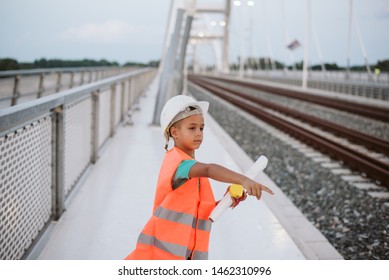 Small workers. An engineer boy with a protective helmet and vest stands on the bridge