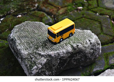 Small Yellow Bus Toy On A Rock.