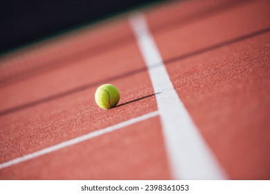 Small yellow tennis ball is lying on tennis court outdoors, sunny weather - Powered by Shutterstock