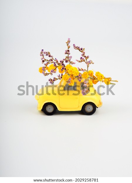 Small yellow toy car with a bouquet of wild\
flowers on a white\
background.