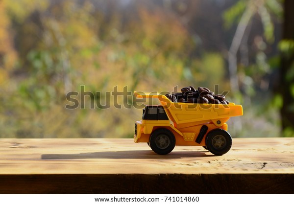 A small yellow toy truck is\
loaded with brown coffee beans. A car on a wooden surface against a\
background of autumn forest. Extraction and transportation of\
coffee