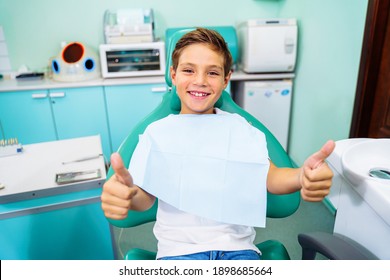 Small, Young Patient Boy Is Happy With A Visit To The Dentist. Concept Of Painless Dental Treatment. Beautiful, Wide Smile Of A Child Sitting In A Dental Chair In A Doctor's Office. Thumbs Up.