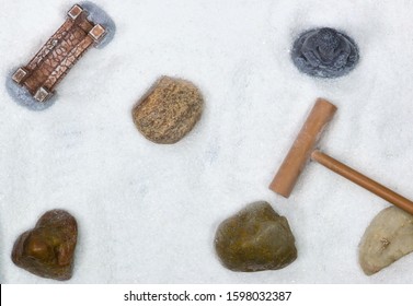 Small Zen Garden With White Sand, A Rake And Scattered Rocks And Ornaments Within With Space Around Them. Full Frame Image As Seen From Directly Above.