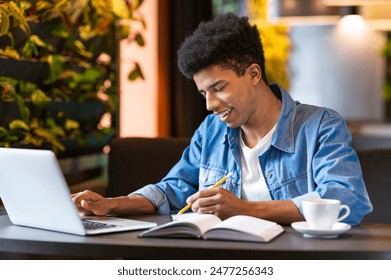 A smart African American young guy is seated at a table, working on a laptop while sipping from a cup of coffee. He appears focused and engaged in his work. - Powered by Shutterstock