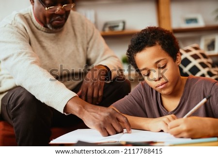 Smart African boy doing his math homework with a little help of his grandpa. Tutoring and education