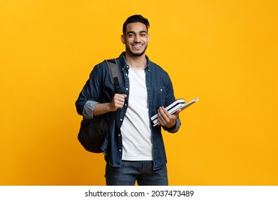 Smart arab guy student with backpack and bunch of books smiling at camera, copy space for advertisement over yellow studio background. Education, university, college, studying, course concept - Shutterstock ID 2037473489